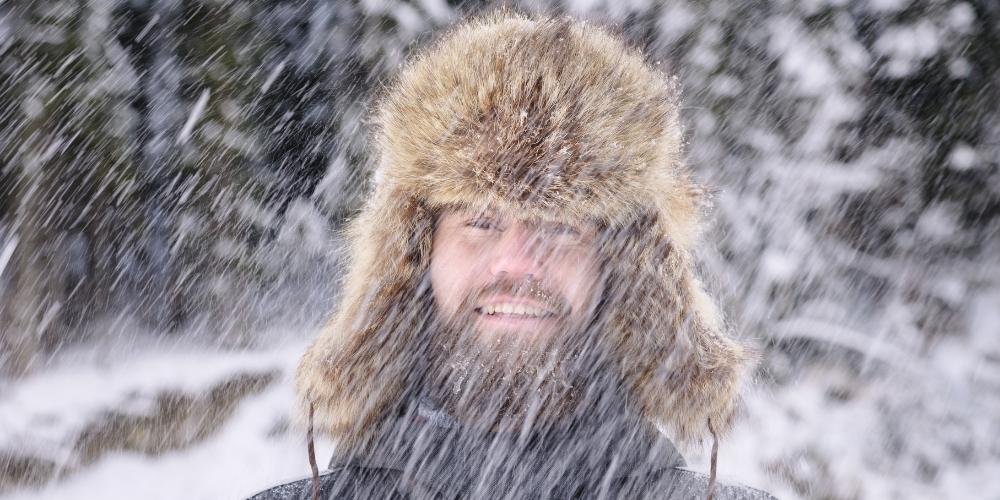 A content man standing outside in the cold as snow pours down on him.