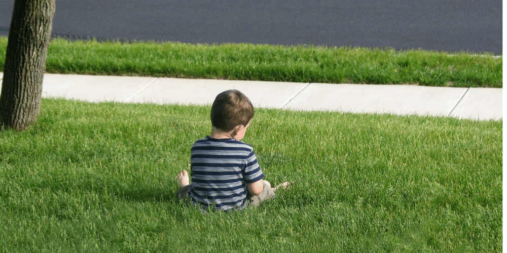 A young boy sitting on the grass, all alone.