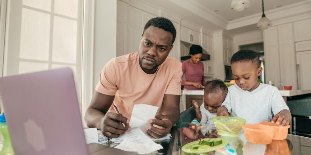 Dad working on his finances while his kids are eating breakfast, and while his wife is working in the kitchen.