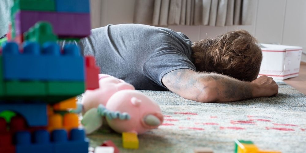 Dad sleeping on the floor surrounded by toys.