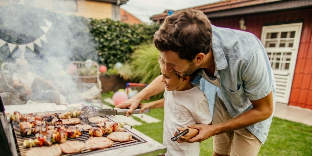 Dad helping his young son grill.