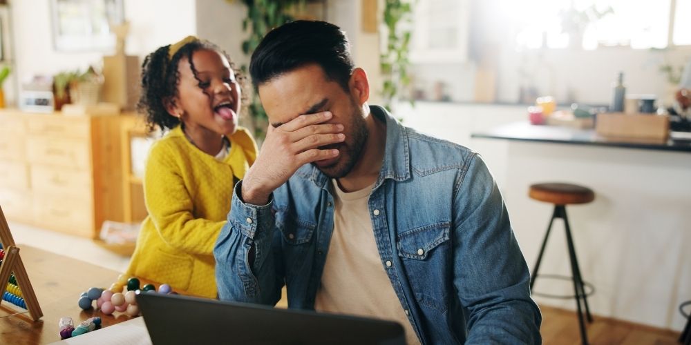 A frustrated dad is sitting at a table, and his kid is trying to get his attention.