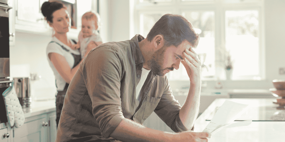 A stressed father looking at a bill he has to pay while his wife and baby look at him.
