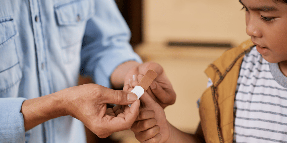 Dad putting a band-aid on his son's thumb.